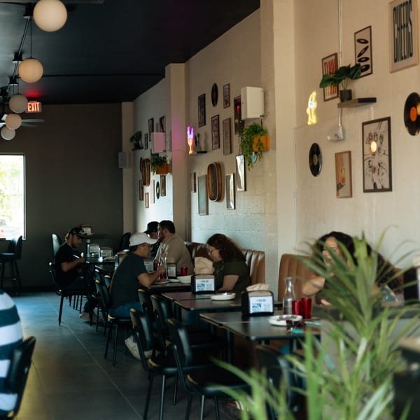 Diners seated at tables and booths in Perla's Pizza, with eclectic wall decor and modern lighting.