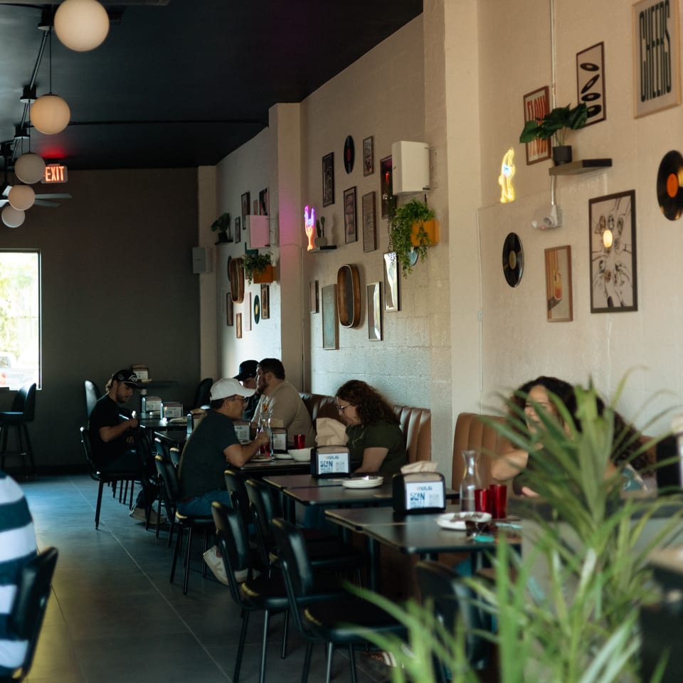 Diners seated at tables and booths in Perla's Pizza, with eclectic wall decor and modern lighting.