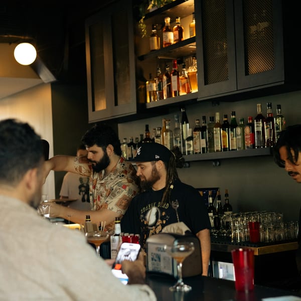 Bartenders in a dimly lit bar, with bottles of liquor on shelves behind them.