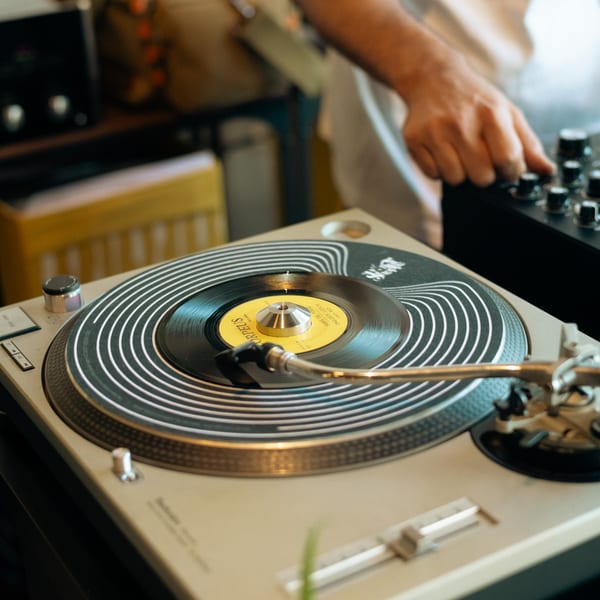 A person's hand adjusts controls on a mixer next to a turntable playing a record.